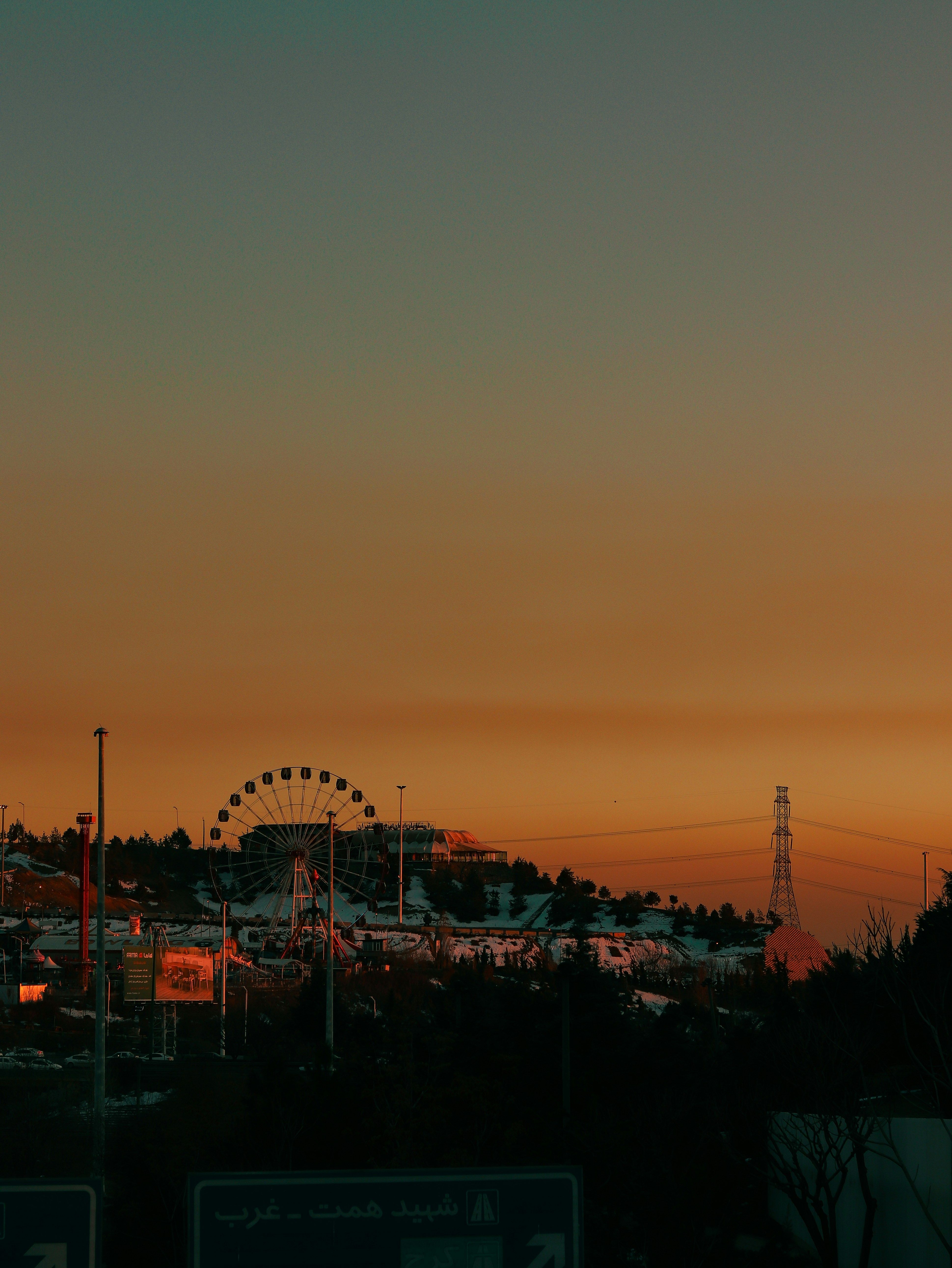 a sunset view of a roller coaster and a ferris wheel