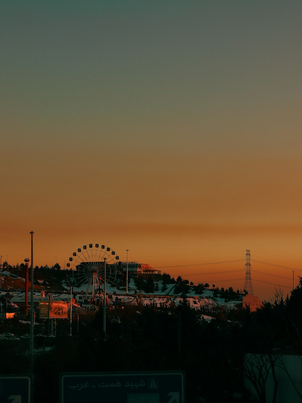 a sunset view of a roller coaster and a ferris wheel