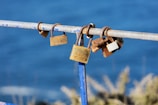 Several rusty padlocks attached to a metal railing with a backdrop of a blurred blue ocean and grassy foreground.