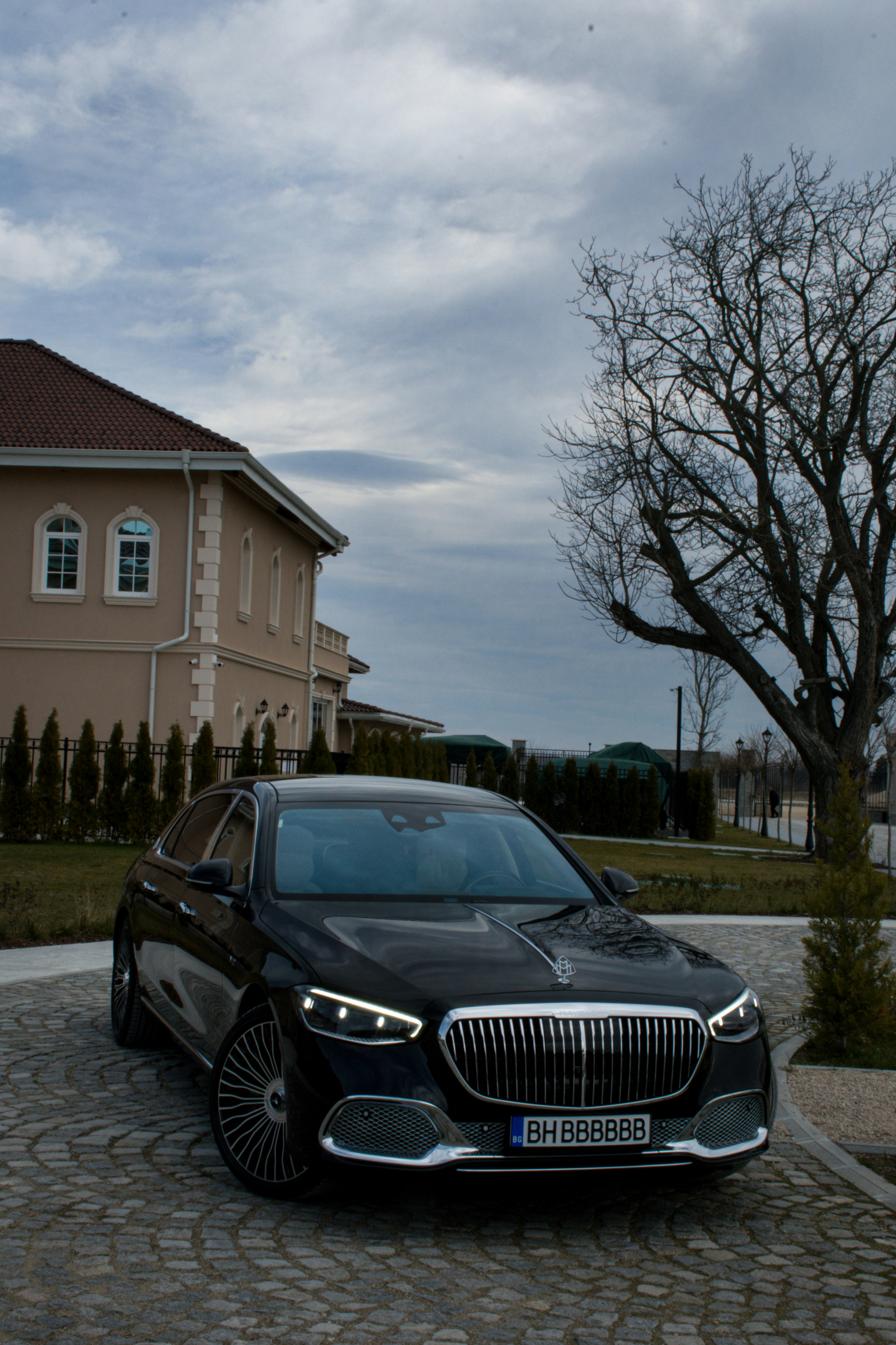 Luxury estate driveway at twilight, warm amber interior glow, dark stone facade, deep shadows, cinematic atmosphere