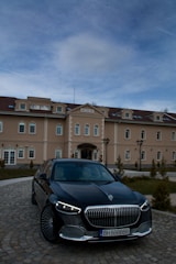 A luxury car is parked in front of an elegant building named 'Bononia'. The building displays classic architectural design with multiple windows and a symmetrical facade. The sky above is partially cloudy.