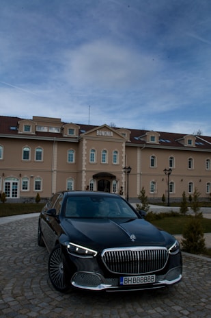 A luxury car is parked in front of an elegant building named 'Bononia'. The building displays classic architectural design with multiple windows and a symmetrical facade. The sky above is partially cloudy.
