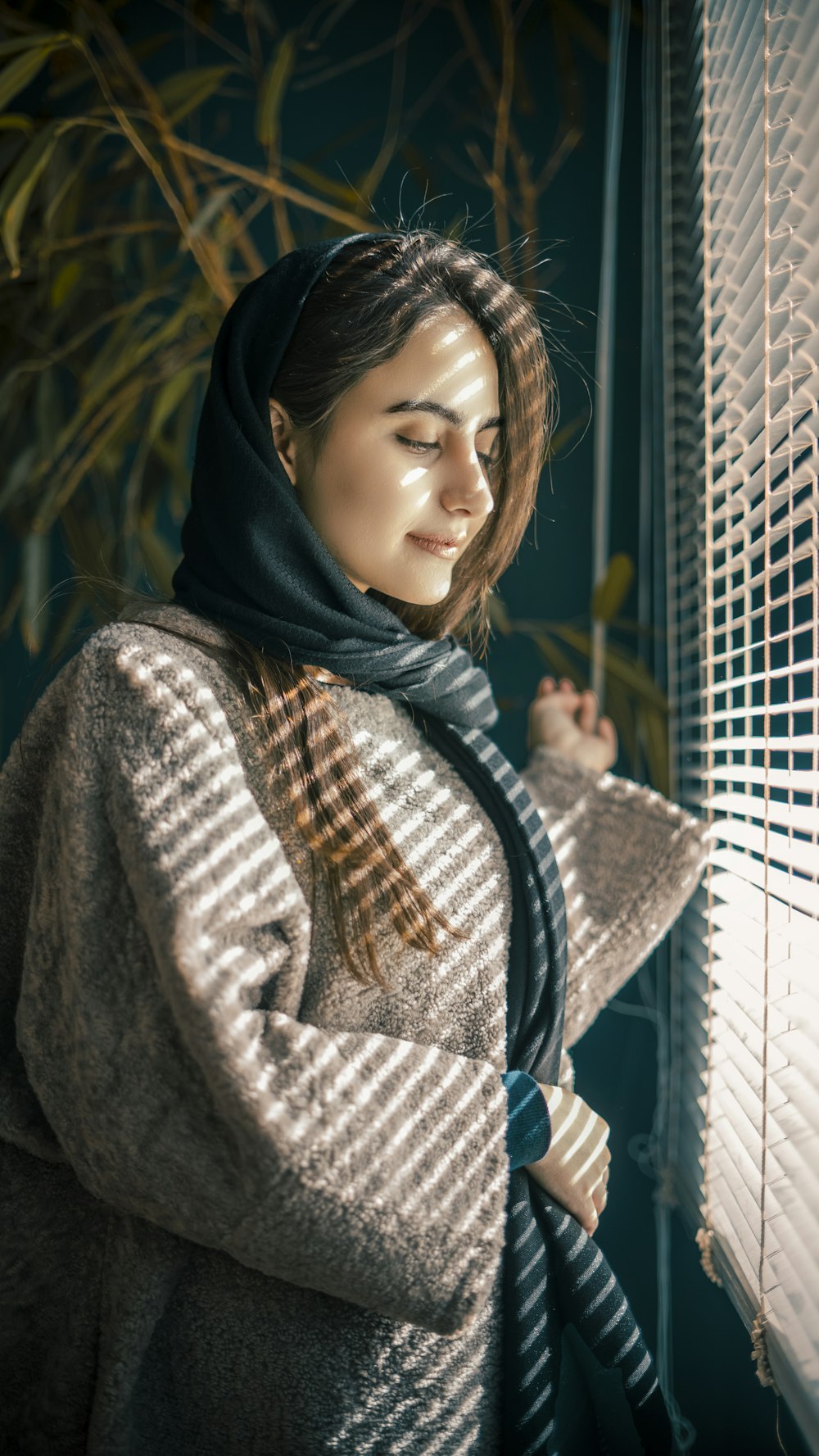 a woman standing next to a window with a scarf on