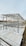 A metal framework structure, likely part of a construction or installation project, is situated near a body of water. The structure comprises numerous horizontal and vertical metal beams, set against an urban backdrop with buildings visible in the distance.
