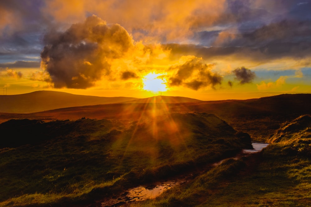 the sun is setting over a grassy hill