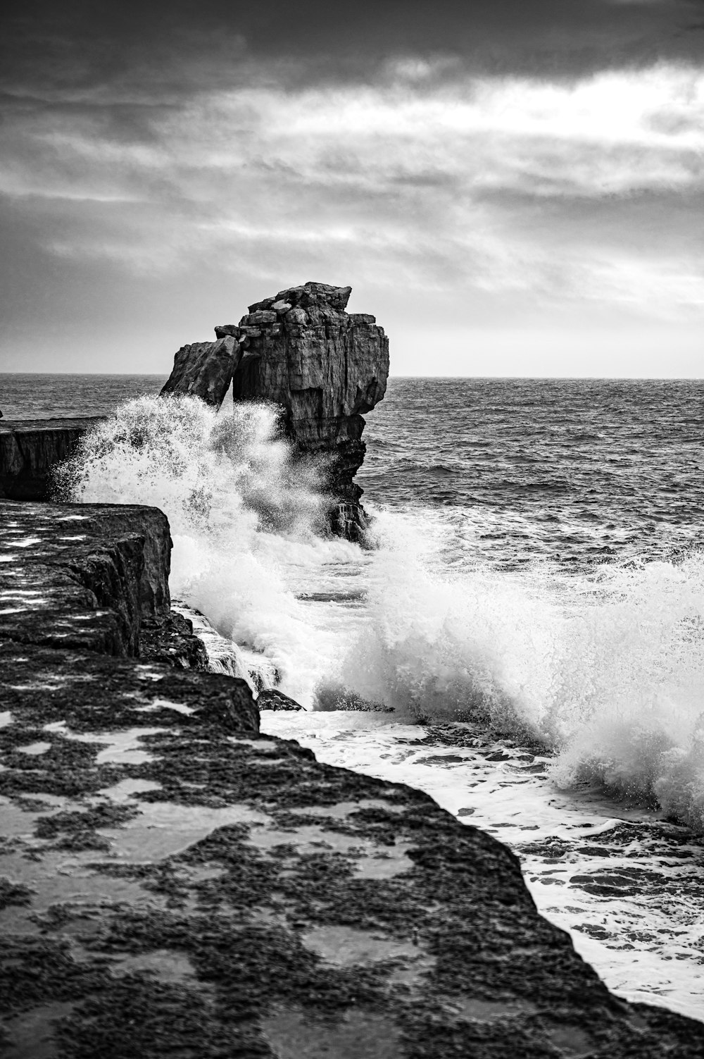 a black and white photo of waves crashing against a rock