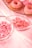An assortment of pink-themed sweets includes frosted donuts, gummy candies, and small candy rolls arranged on a light pink tablecloth.