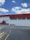 A red and white industrial building with the letters 'C4' prominently painted on the upper section. A red truck is parked beside the building on a paved area, and there is a small speed limit sign indicating 20 km/h nearby. The sky is blue with scattered fluffy clouds.