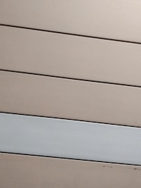 Horizontal panels with a matte finish are arranged in parallel. The panels are mostly beige with one grayish-white panel standing out against the rest.
