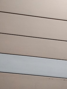Horizontal panels with a matte finish are arranged in parallel. The panels are mostly beige with one grayish-white panel standing out against the rest.