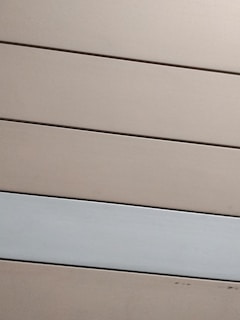 Horizontal panels with a matte finish are arranged in parallel. The panels are mostly beige with one grayish-white panel standing out against the rest.