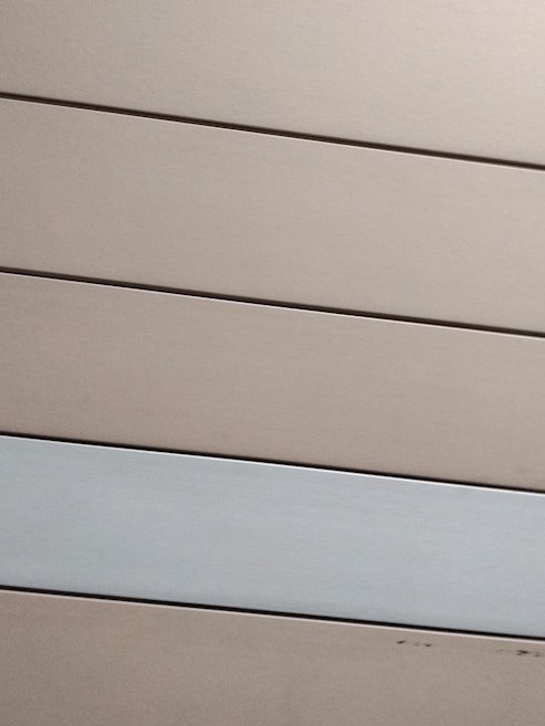 Horizontal panels with a matte finish are arranged in parallel. The panels are mostly beige with one grayish-white panel standing out against the rest.