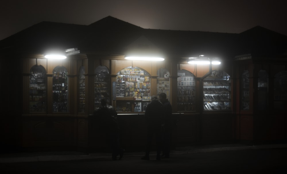 a couple of people standing outside of a store at night