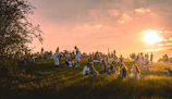 a group of people sitting in a field at sunset