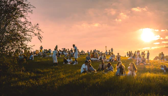 a group of people sitting in a field at sunset