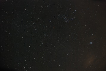A vast expanse of dark night sky filled with numerous small, bright stars scattered across the image. Some stars form recognizable patterns, indicative of constellations. The backdrop is a deep black with subtle hints of blue and purple hues, adding to the cosmic feel.