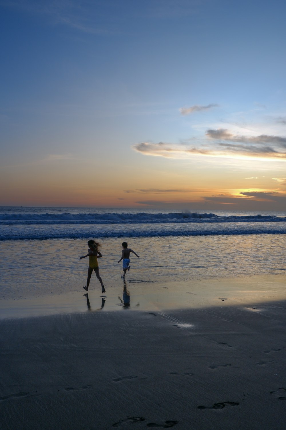 two children running on the beach at sunset