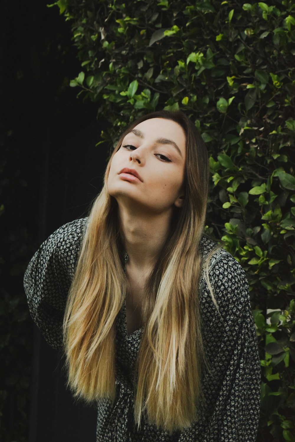 a woman with long hair standing in front of a bush