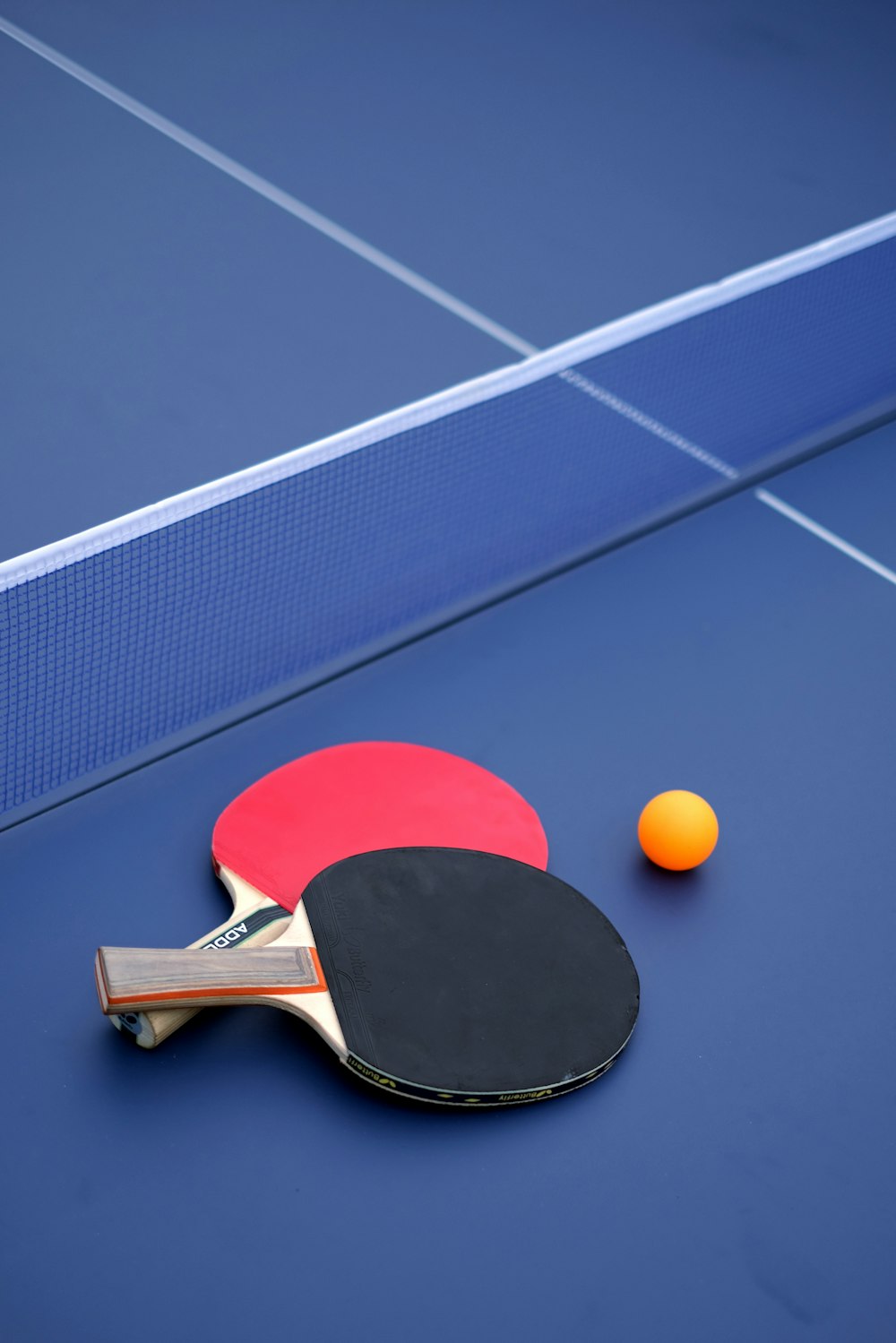 two ping pong paddles and an orange ball on a blue table