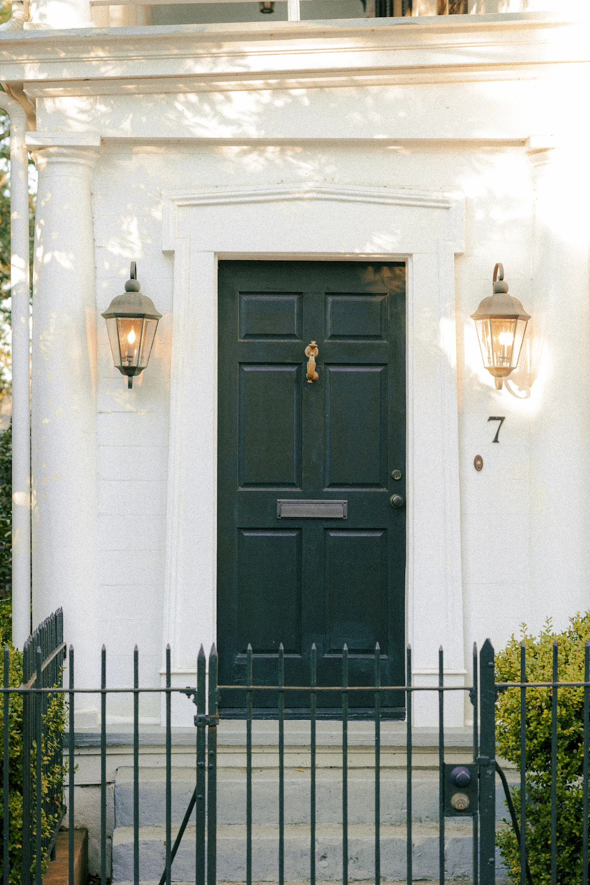 Paneled front door framed by two lanterns on a white facade