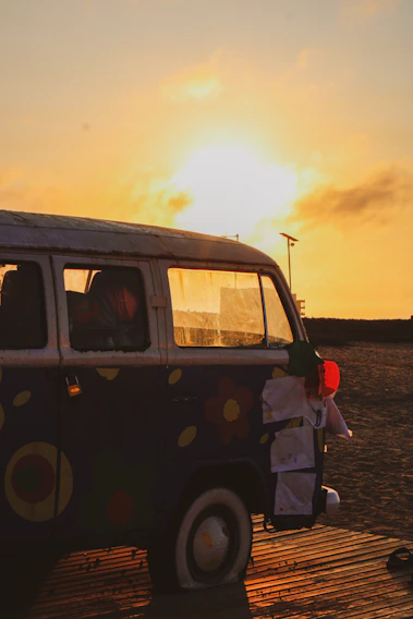 A vibrant sunset over a serene beach with a colorful kombi van parked nearby.