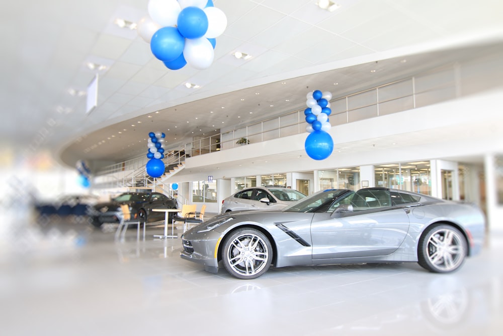 um carro esportivo prateado em um showroom com balões azuis e brancos
