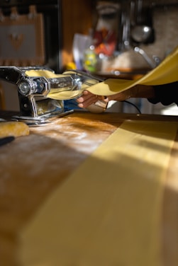 Close-up of fresh pasta being rolled out on a wooden board in a cozy kitchen.