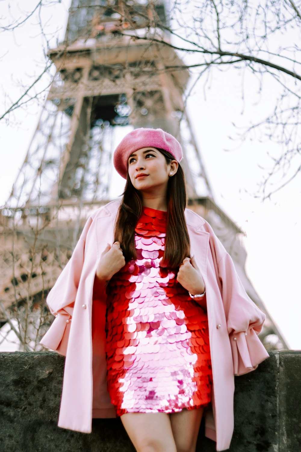 a woman in a red dress and pink coat standing in front of the eiff