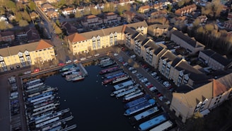 Aerial view of a residential area with several apartment buildings surrounding a marina filled with narrowboats. The buildings are arranged in a U-shape, and the marina is enclosed within this formation. Cars are parked along the streets next to the buildings. The area is surrounded by roads and other residential neighborhoods, with some trees interspersed.