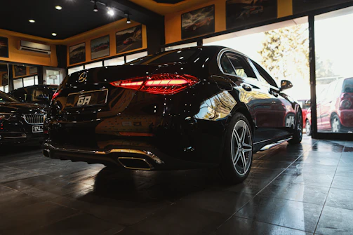 A sleek black luxury car parked outside a modern showroom under warm lighting.