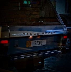 A vintage Range Rover with a Dubai license plate parked in a dimly lit area. The car's back shows the model name 'Vogue SE' and the plate number '22000'.