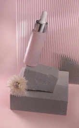 Soft pastel pink and beige cosmetic bottles arranged elegantly on a white marble surface with natural flowers.