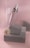 A soft pink and gray composition featuring a cosmetic dropper bottle resting on textured gray blocks. A delicate white flower lies next to the blocks. The background consists of a corrugated pink surface, enhancing the aesthetic appeal with subtle shadows.