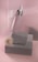 A soft pink and gray composition featuring a cosmetic dropper bottle resting on textured gray blocks. A delicate white flower lies next to the blocks. The background consists of a corrugated pink surface, enhancing the aesthetic appeal with subtle shadows.