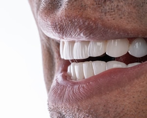 Close-up of a smiling person holding a Prodentim probiotic chew near their mouth, surrounded by fresh strawberries and peppermint leaves.