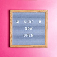 a sign that says shop now open on a pink wall