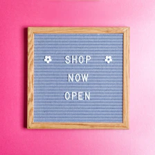 a sign that says shop now open on a pink wall