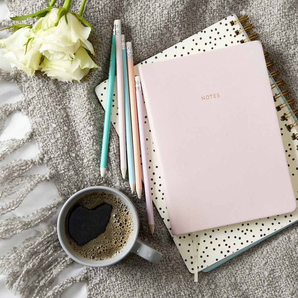 a cup of coffee next to a notebook and pencils