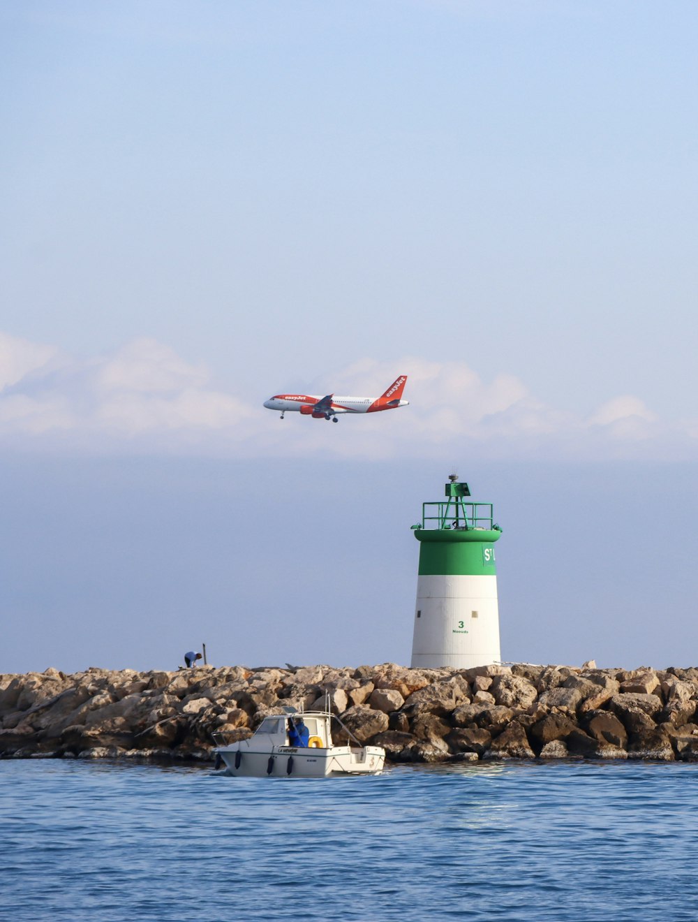 a plane flying over a light house in the ocean