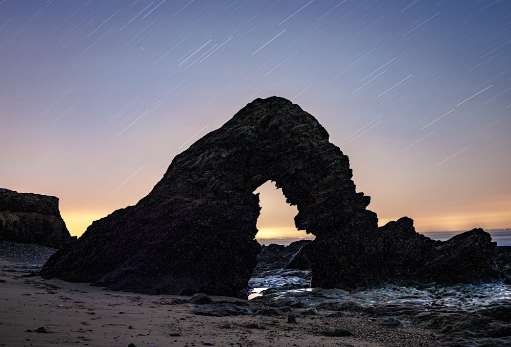 a rock formation on a beach with a star trail in the sky