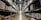 A large warehouse aisle flanked by tall metal shelves filled with stacked boxes and packages. The shelves extend towards the back of the warehouse, where they converge in the distance. The lighting is bright and industrial, with fluorescent lights illuminating the space.