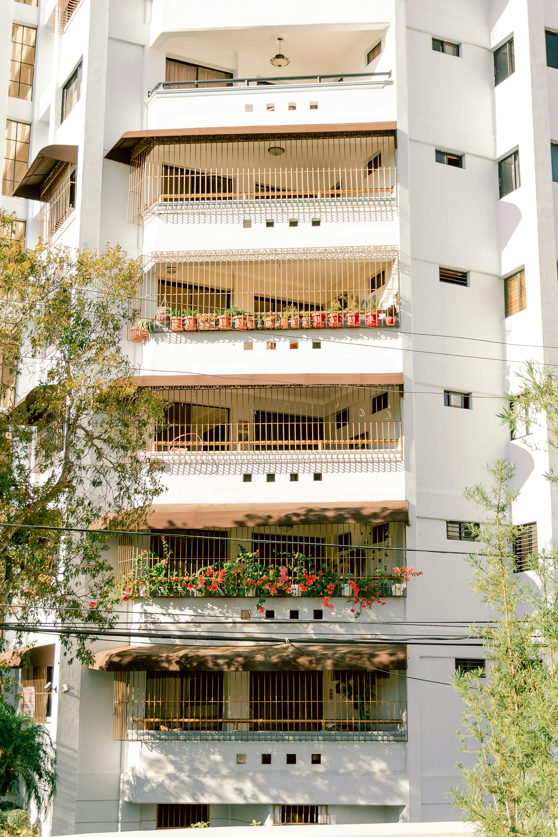 a tall white building with balconies and flowers on the balconies