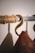 A close-up of a brass hook attached to a metal rod wrapped with rope. A leather item hangs from the hook, casting a shadow on the textured wall, highlighting the craftsmanship of the materials.