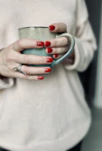 Close-up of rose pink nail polish on perfectly manicured hands holding a coffee cup.