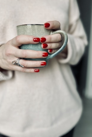 Close-up of hands with a fresh manicure holding a cup of coffee.