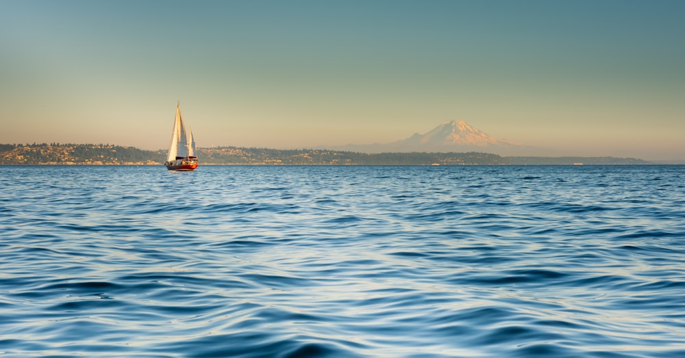 a sailboat in the ocean with a mountain in the background