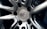 A close-up view of a polished metal car wheel hub with intricate design patterns. The central area features a circular logo with letters and text indicating manufacturing details. The surfaces are smooth and reflective, highlighting the craftsmanship of the metalwork.