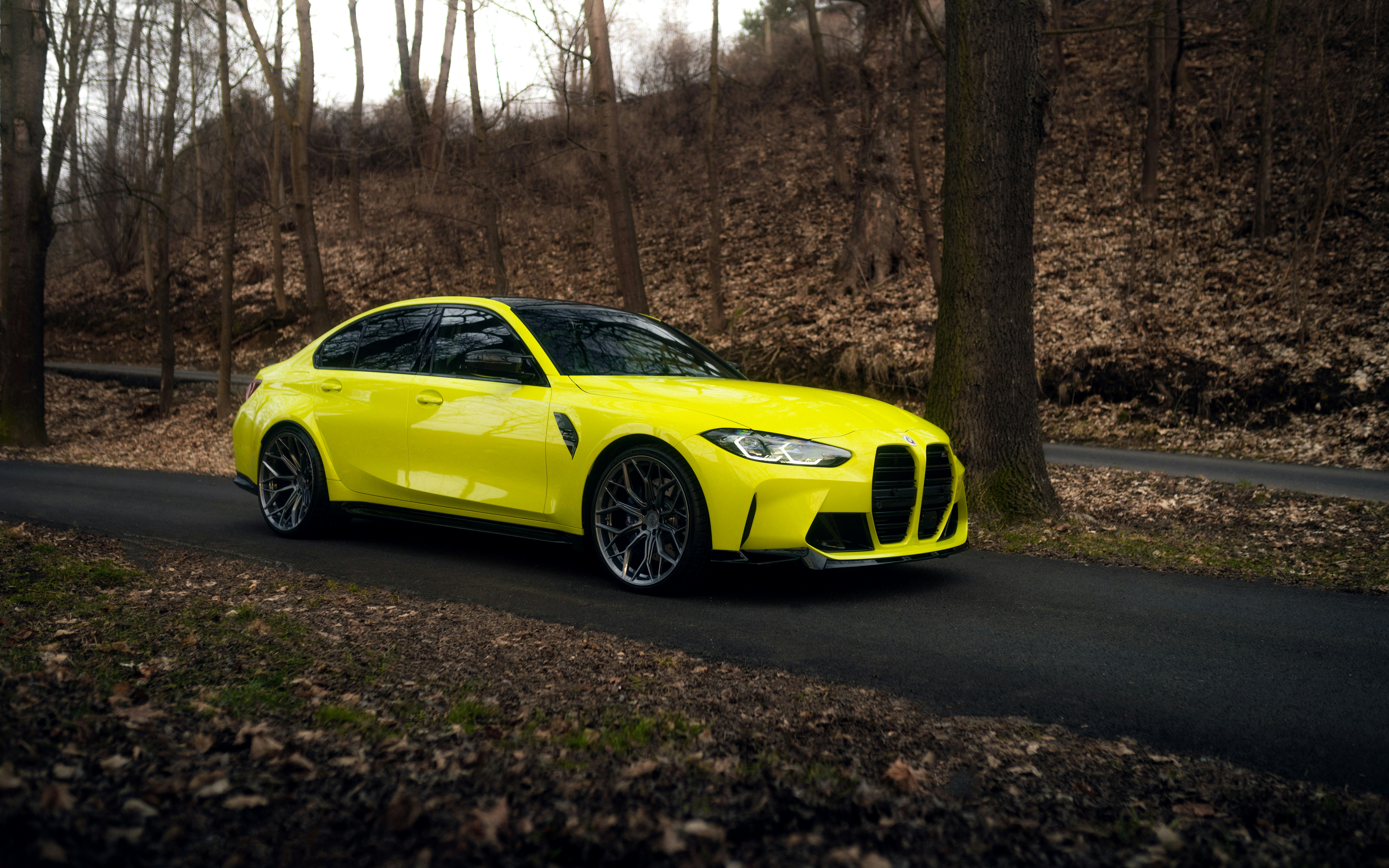 A yellow sports car driving down a road in the woods photo – Free ...