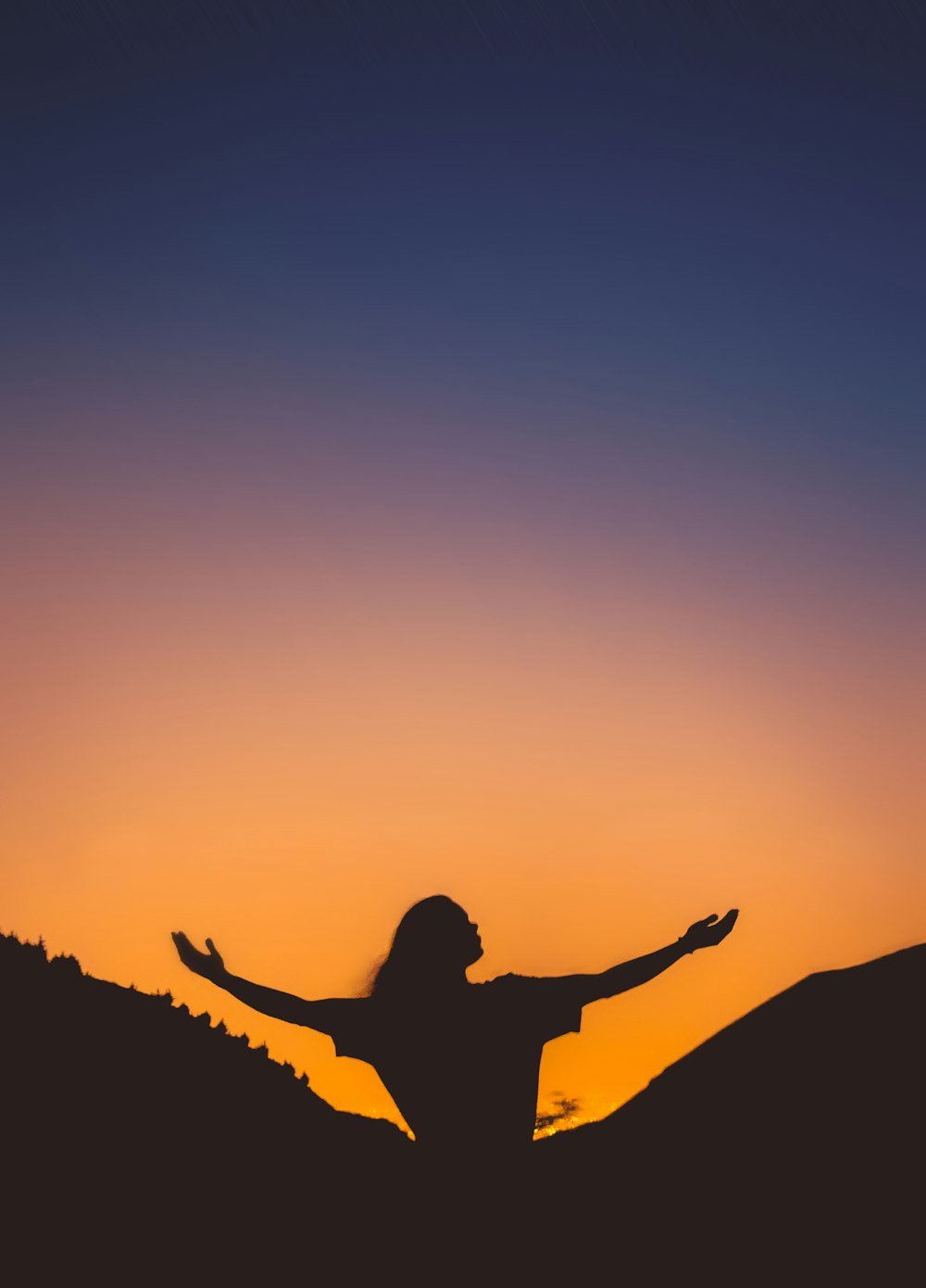 a woman standing on top of a hill with her arms outstretched