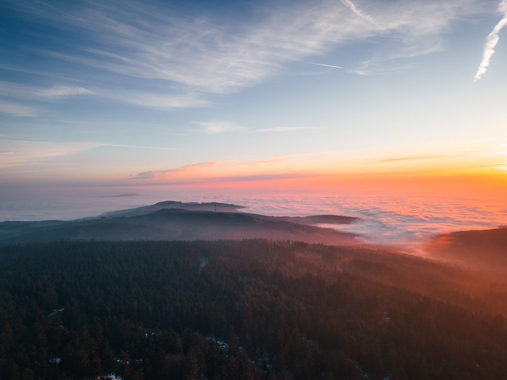 the sun is setting over a foggy mountain